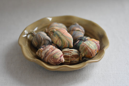 Jemma Lewis colourful marbled wooden acorn decoration Christmas ornaments, in a wavy ceramic bowl on a beige background.