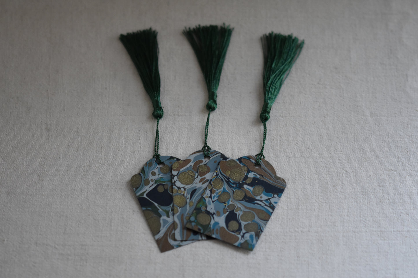 Jemma Lewis set of 3 marbled blue and green gift tags with green tassels on a beige background.