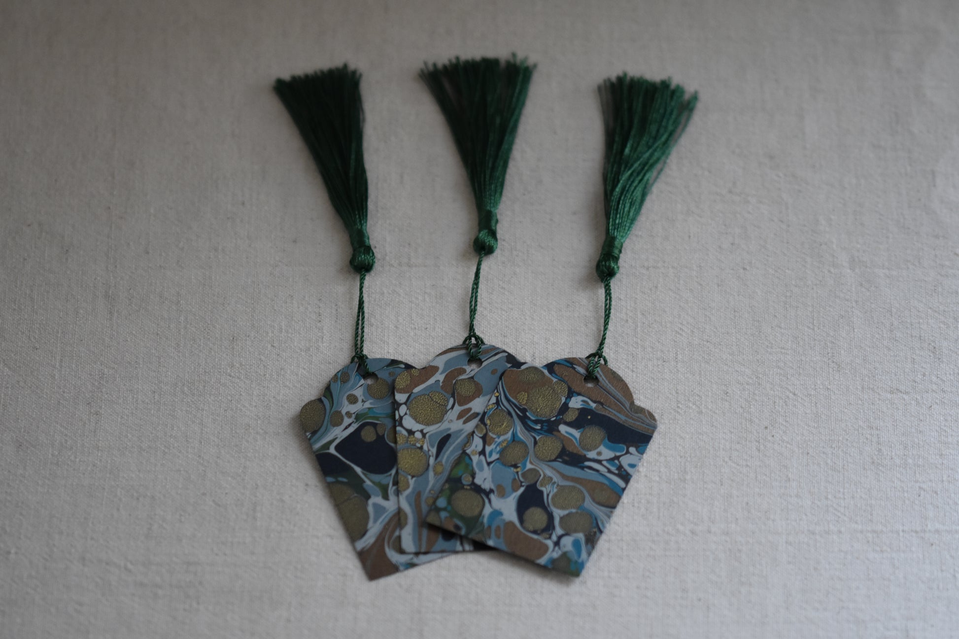 Jemma Lewis set of 3 marbled blue and green gift tags with green tassels on a beige background.