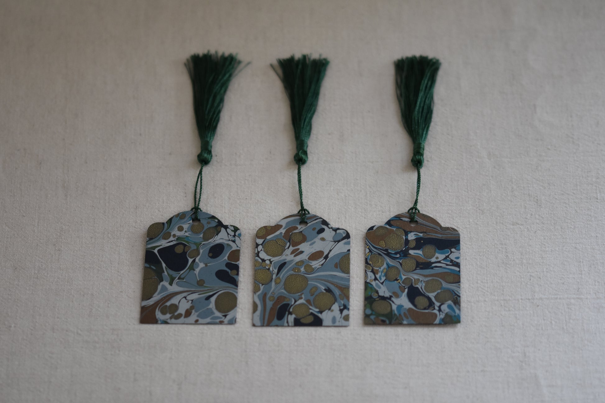 Jemma Lewis set of 3 marbled blue and green gift tags with green tassels on a beige background.