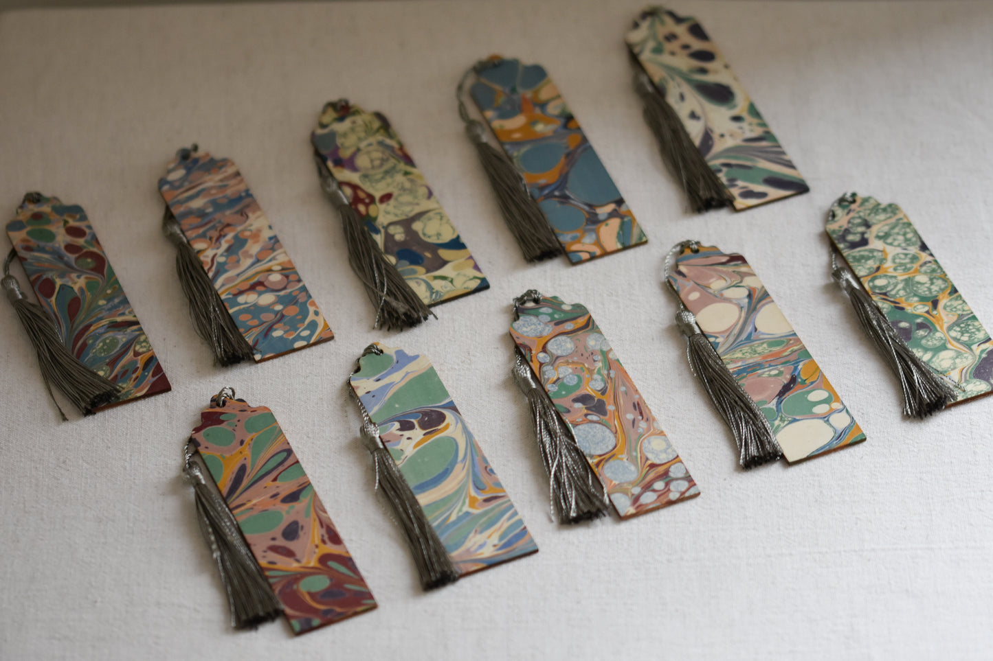 Jemma Lewis colourful marbled wooden bookmarks with grey tassels on a beige background.