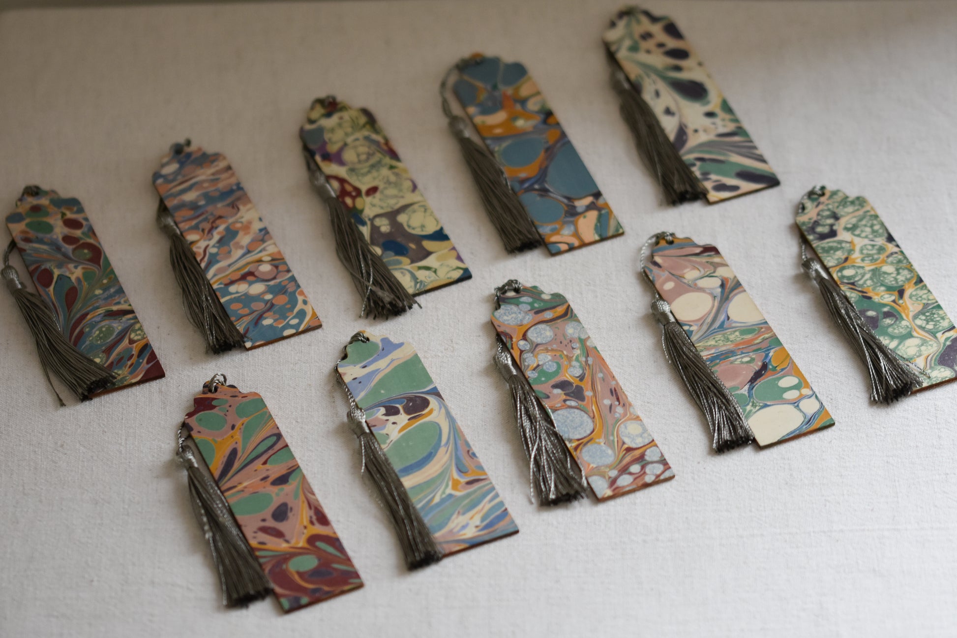 Jemma Lewis colourful marbled wooden bookmarks with grey tassels on a beige background.