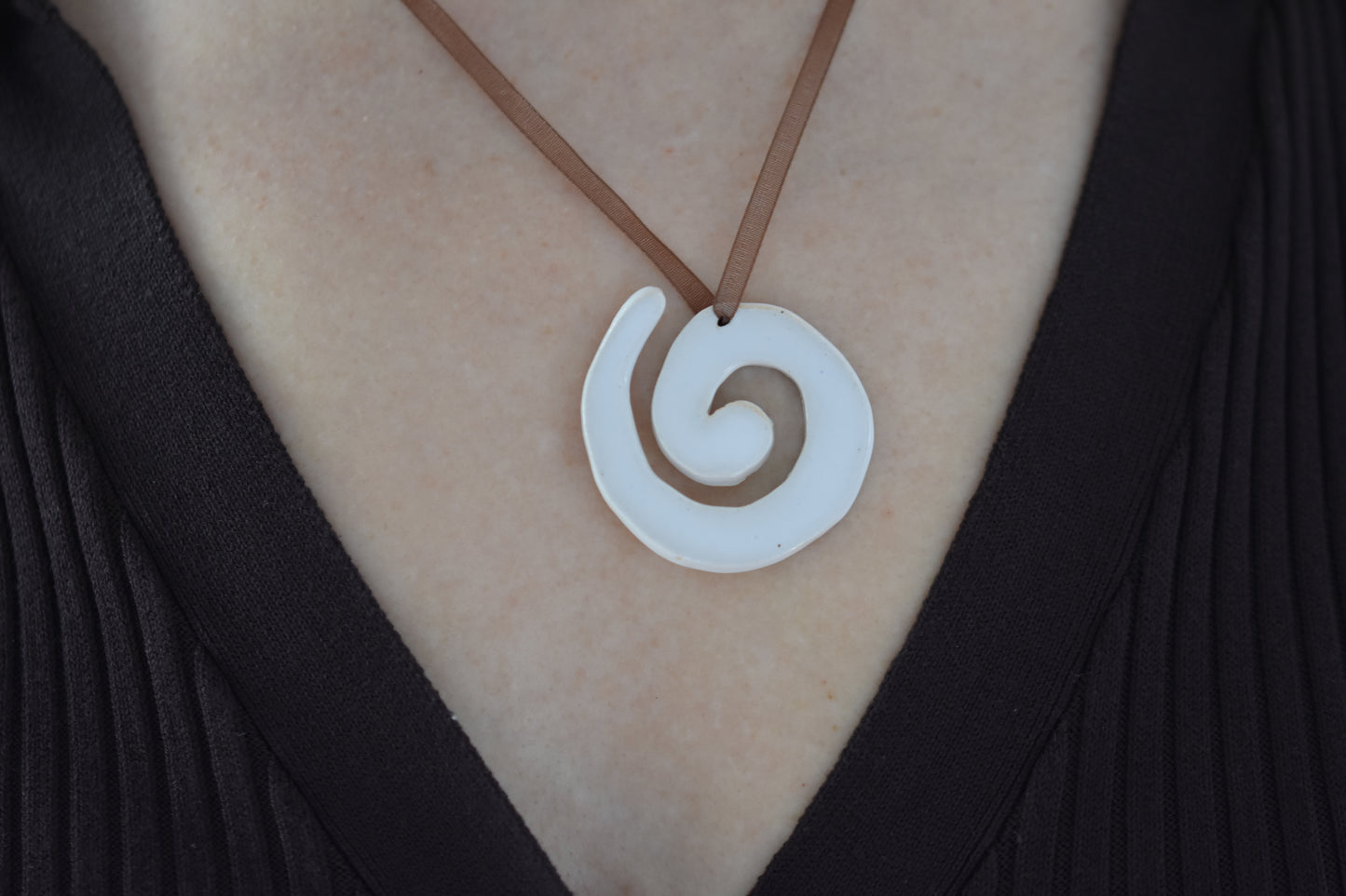 AEA Studio white mini stoneware ceramic swirl spiral pendant on a brown ribbon necklace.