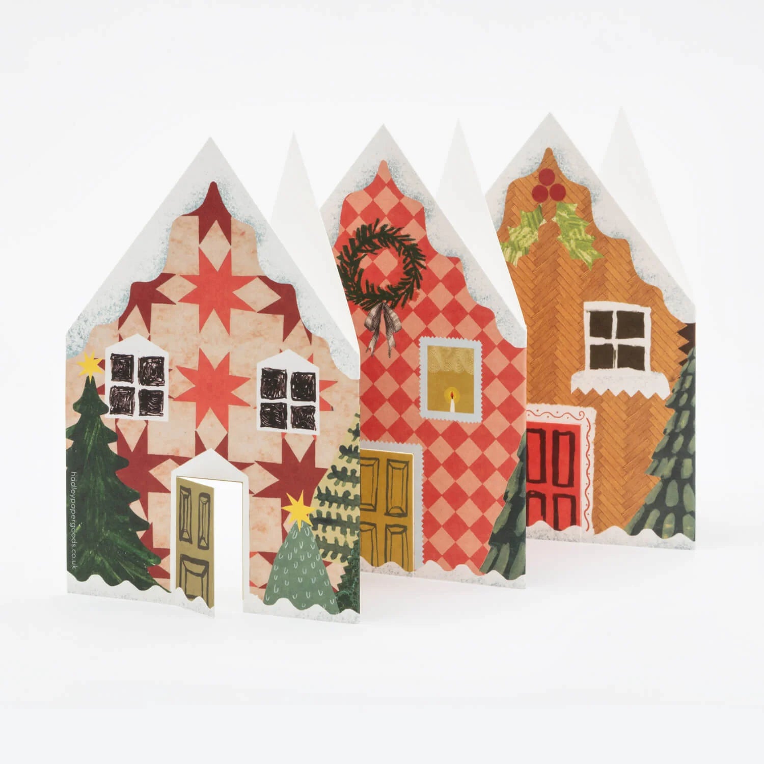 Hadley Paper Goods Concertina Christmas houses card, showing 3 decorative houses, in shades of red and green, on a white background.