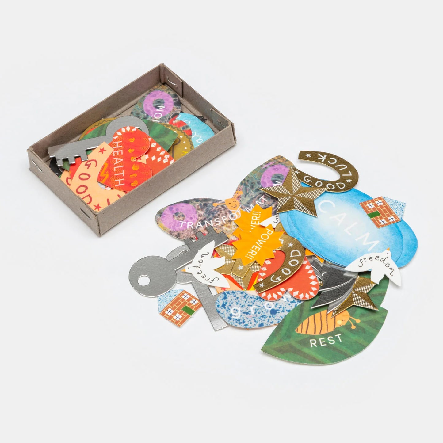 Hadley Paper Goods Manifestation Charms, multicolour card shapes including  hearts, horseshoes and houses, in a grey box on a white background.