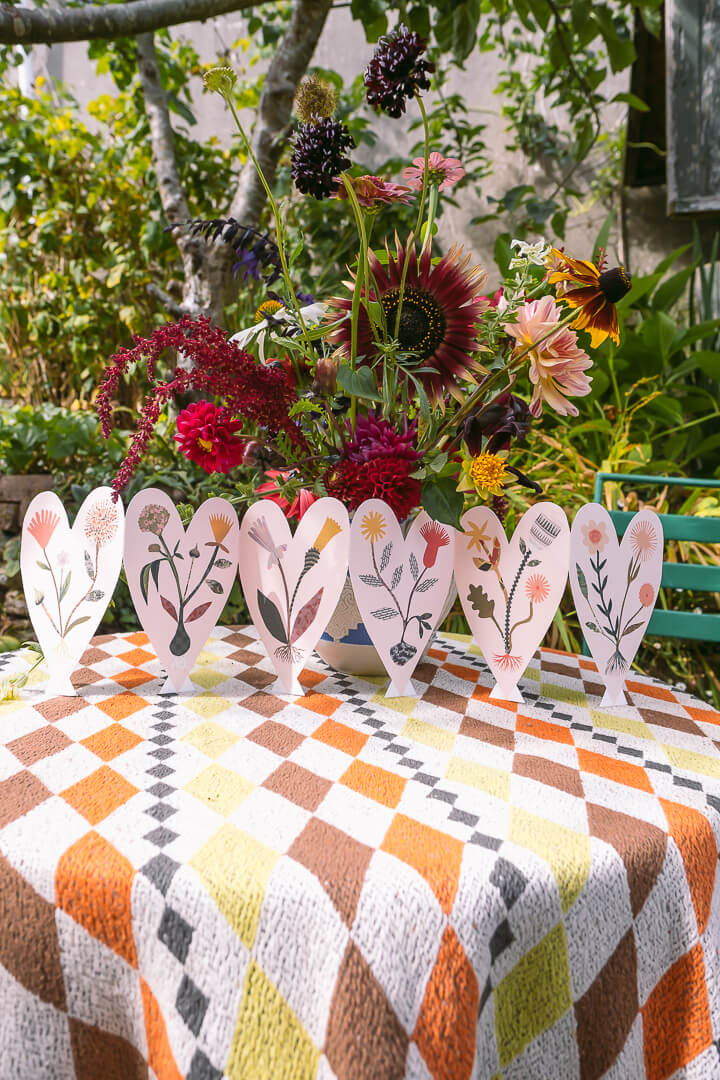 Hadley Paper Goods pale pink heart concertina card of six hearts with wild flowers on a colourful garden table with flowers.