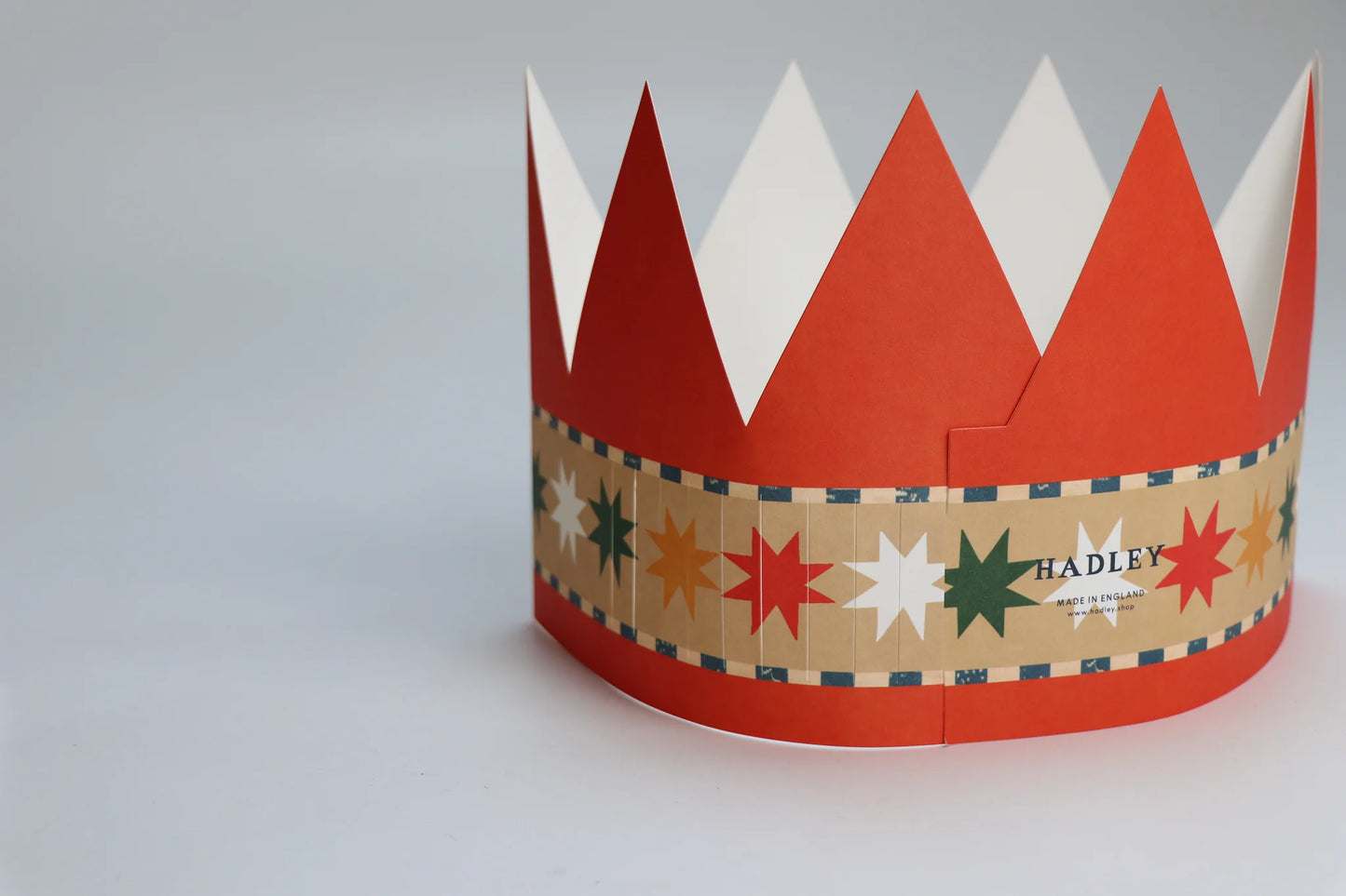 Hadley Paper Goods Chief Elf party hat crown shaped card in orange with blue pattern and multicoloured stars, back view, on a white background.