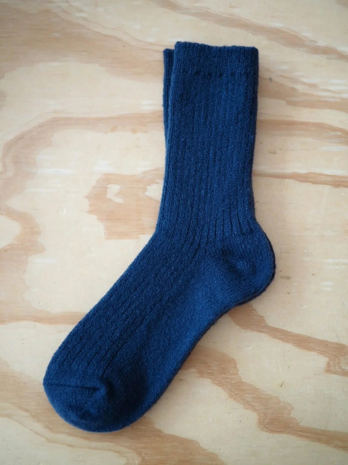 A pair of navy blue ribbed knit Merino wool socks laid flat on a light wood surface.
