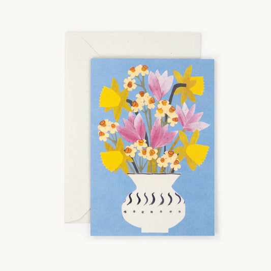 Hadley Paper Goods Spring flowers card showing a bouquet of daffodils, narcissus and tulips in a vase on a cornflower blue background with a cream envelope, on a white background.