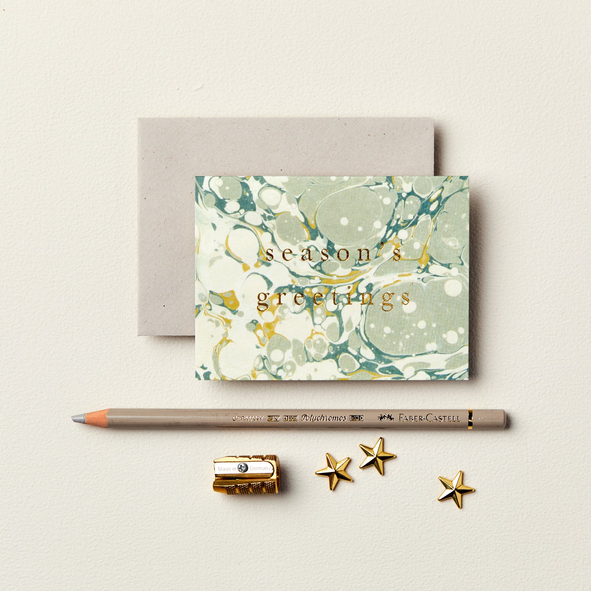 Wanderlust Paper Co. mini cream and green marble card with season's greetings in gold, shown next to stationery on a pale grey background.