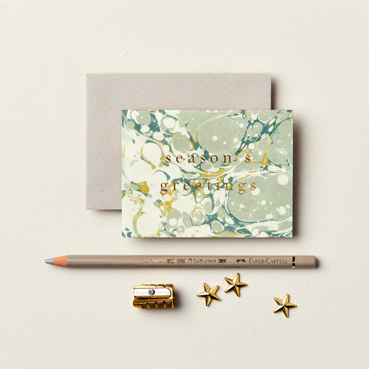 Wanderlust Paper Co. mini cream and green marble card with season's greetings in gold, shown next to stationery on a pale grey background.