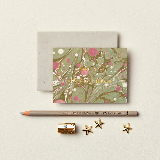 Wanderlust Paper Co. mini green and red marble card with Merry Christmas in gold, shown next to stationery on a pale grey background.