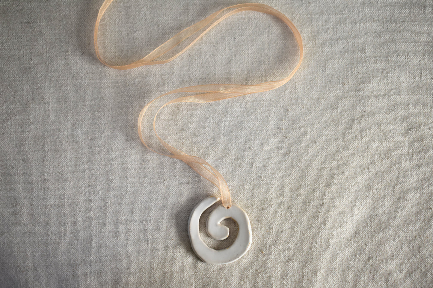 AEA Studio white mini stoneware ceramic swirl spiral pendant on a beige ribbon necklace.