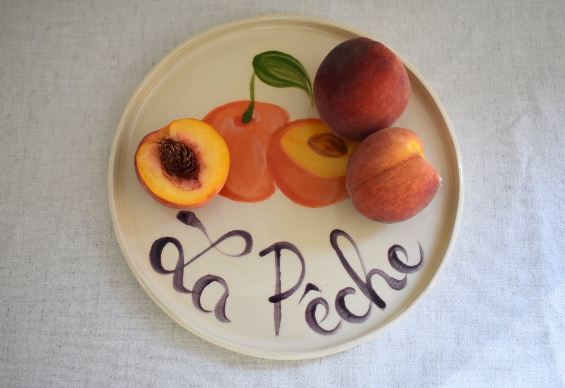 Harlie Brown earthenware ceramic La Peche plate with painted peach design and french writing.