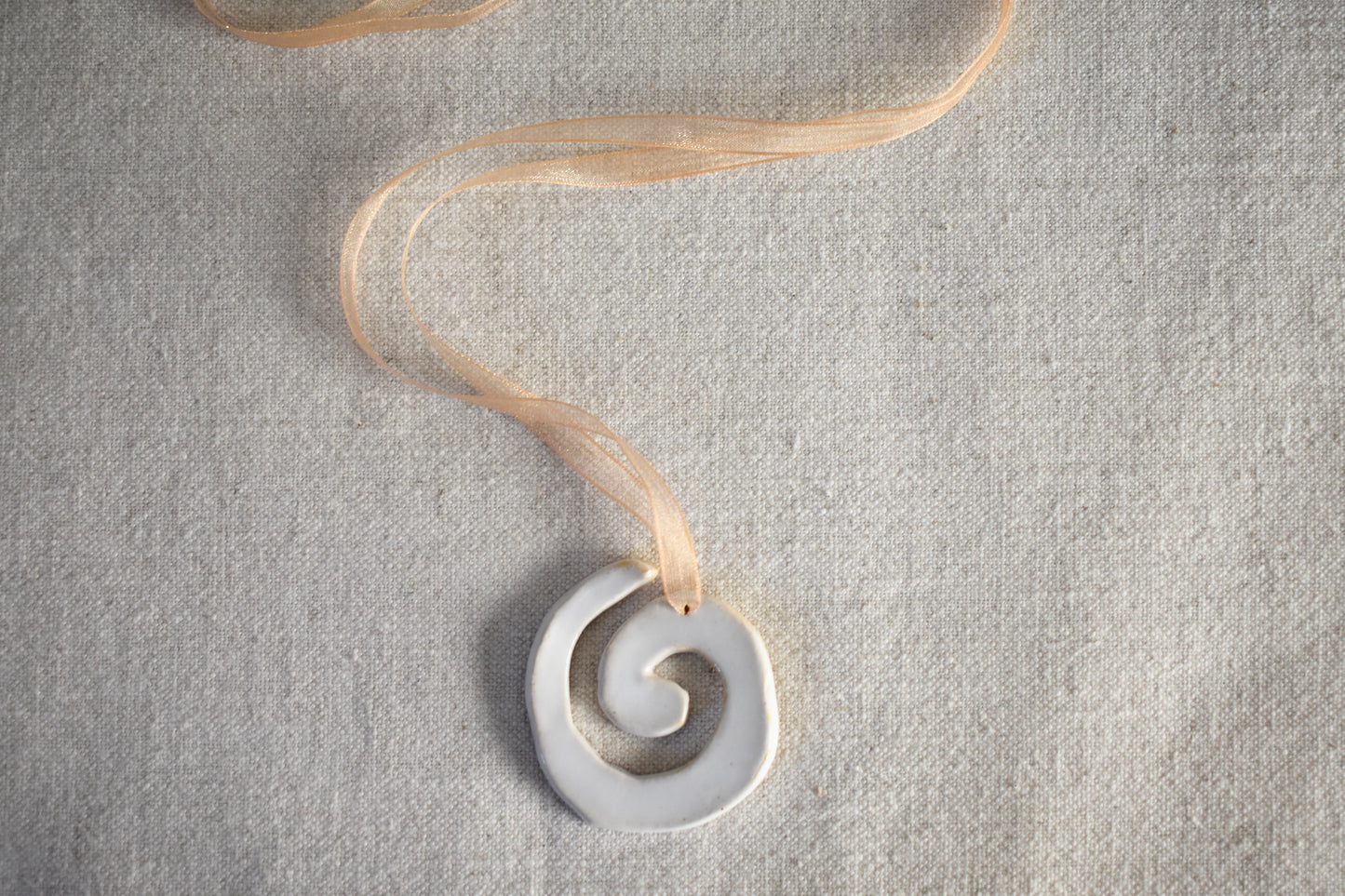 AEA Studio white mini stoneware ceramic swirl spiral pendant on a beige ribbon necklace.